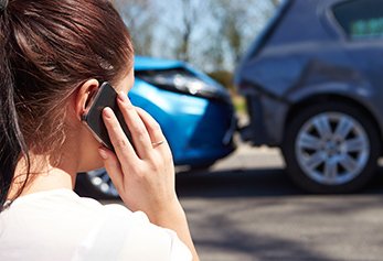 woman on cell phone with car accident in background